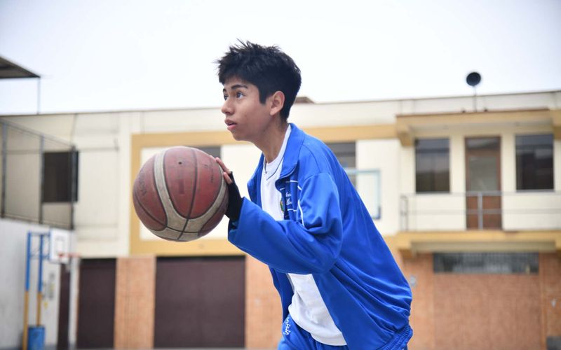 Estudiante de secundaria con buzo azul sujetando el balón de básquet