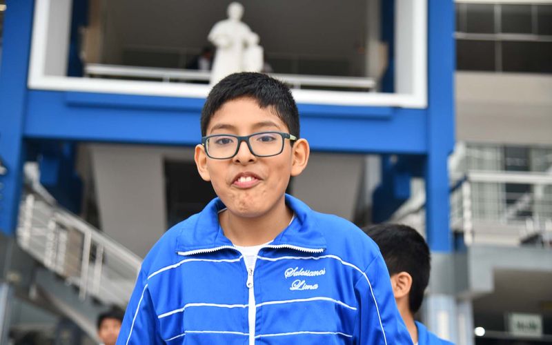 Niño de primaria con lentes y buzo azul sonriendo en el patio