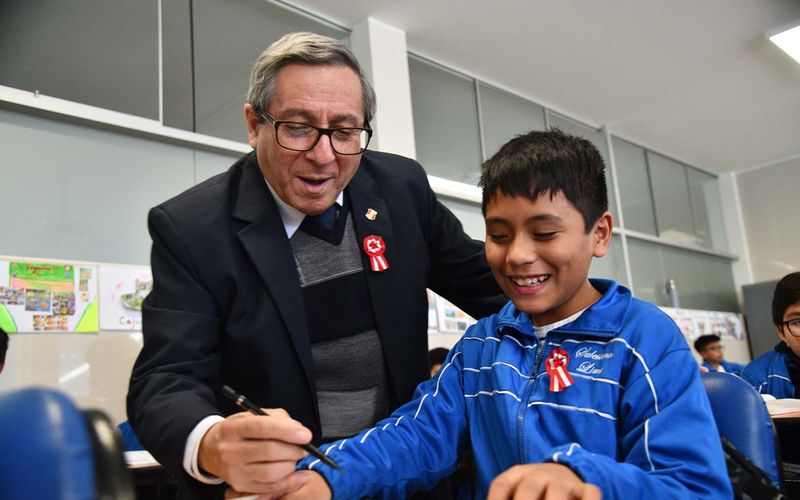 Docente guiando a un estudiante de sexto de primaria mientras escribe en su carpeta
