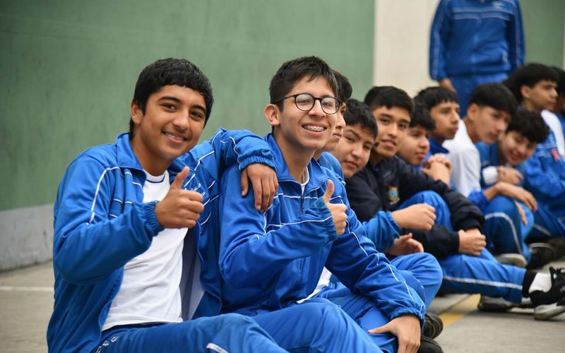 Estudiantes de secundaria con buzo sentados en el patio sonriendo con el pulgar en alto