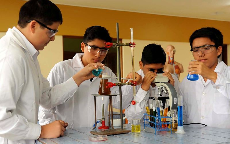 Estudiantes con mandil trabajando con probetas y microscopio en el laboratorio