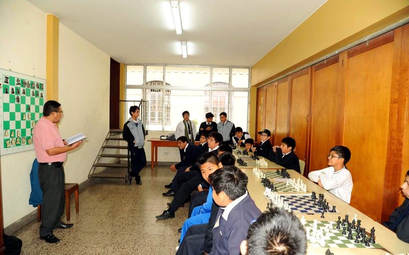 Estudiantes jugando ajedrez en una sala con tableros alineados