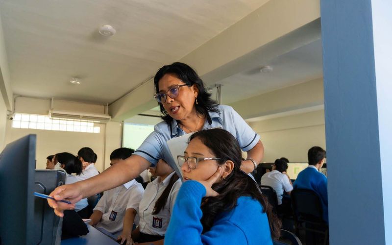 Docente apoyando a una estudiante frente a la computadora en el aula de cómputo
