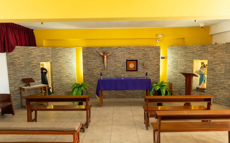 Capilla del colegio con altar, crucifijo y bancas de madera