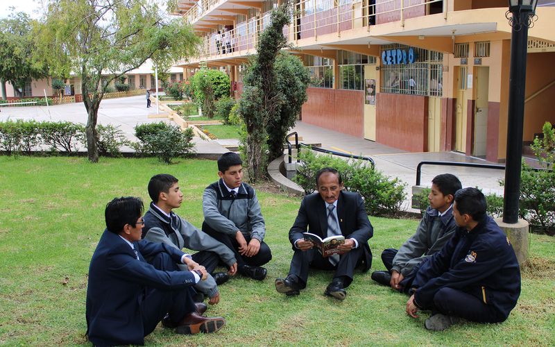 Docente leyendo con un grupo de alumnos sentados en el pasto del patio