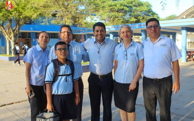 Cuatro docentes abrazando a un alumno de primaria con mochila en el patio