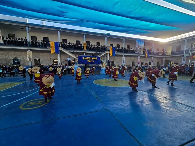 Danzantes con trajes típicos bailan en el patio del colegio bajo un toldo azul