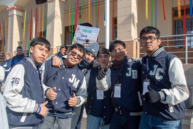 Estudiantes con chaquetas de promoción posan con el pulgar en alto frente al letrero del taller de tecnología