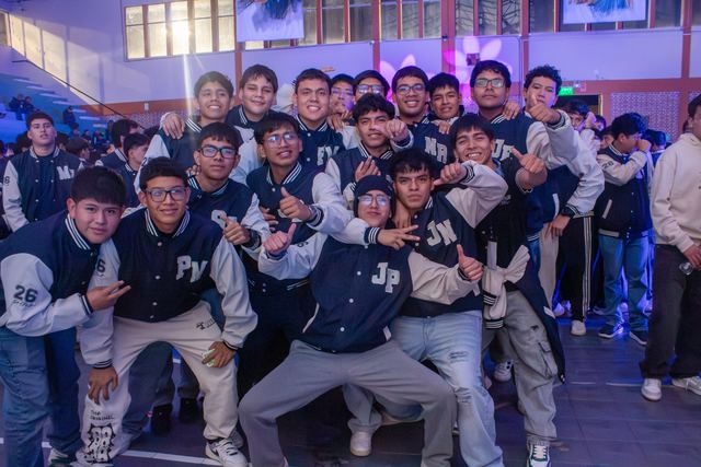 Grupo numeroso de estudiantes con chaquetas de promoción posando en el coliseo