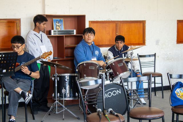 Tres estudiantes ensayan con bajo y batería en un taller de música