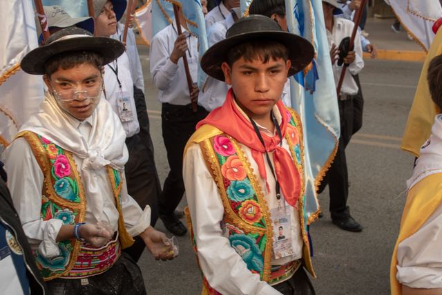 Dos jóvenes con chalecos tradicionales bordados desfilan por la calle
