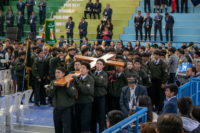 Jóvenes cargan la cruz de madera entre estudiantes con uniformes verdes