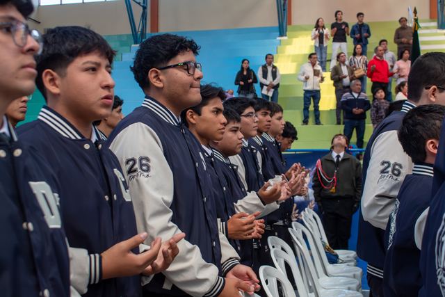 Jóvenes con chaquetas de promoción participan de la Eucaristía con las manos en oración